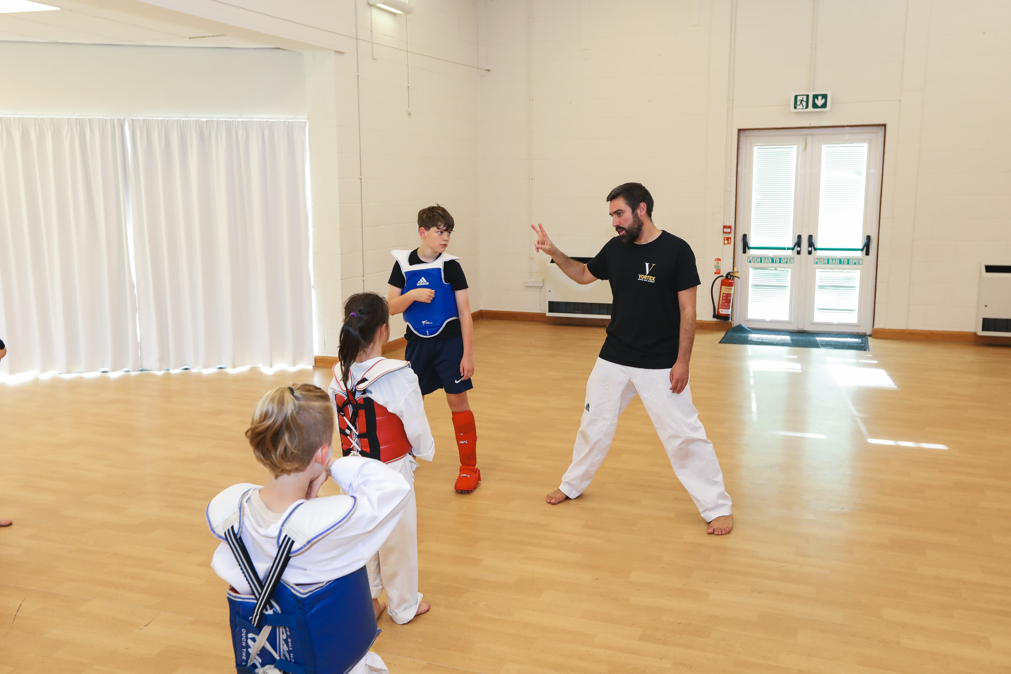 Taekwondo class at Vortex Martial Arts Academy, coach guiding students through sparring drills in protective gear